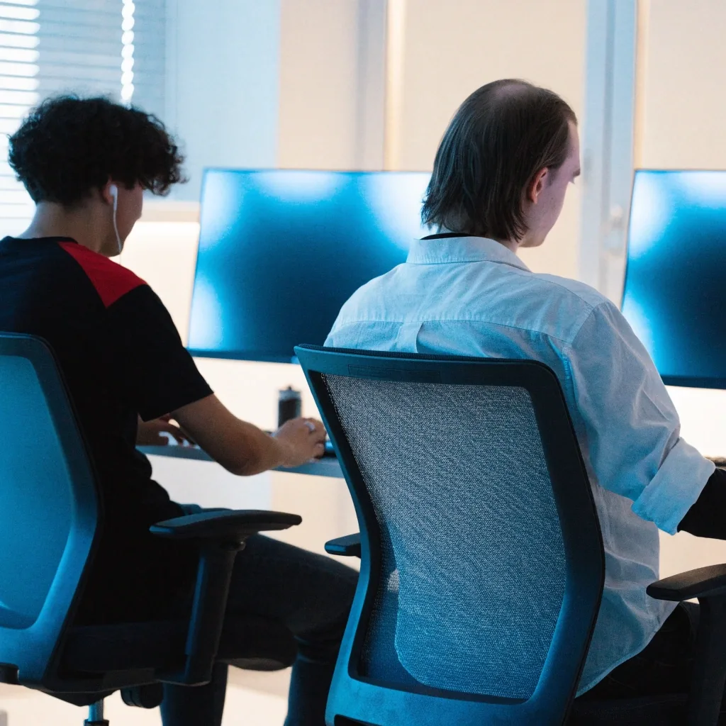 Two players in front of bright monitors without readable content, seen from behind